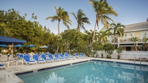 A swimming pool with blue lounge chairs and umbrellas, surrounded by palm trees and a white fence. - Shipyard 208-6 Condo in Truman Annex-2 bedroom 2 bath, close to Duval w/ pool (Key West)