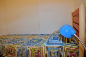 Un lit recouvert d’une couvre-lit aux motifs géométriques colorés, avec une lampe de chevet bleue.