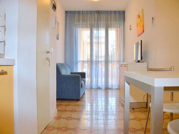 Une pièce avec un canapé bleu, une table blanche et un téléviseur posé sur un meuble.