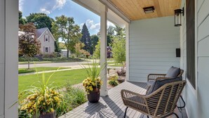 A covered porch with a wicker chair and a potted plant. - Cherry Pie Abode | Walkable to Downtown Boyne | Pet Friendly | Hot Tub (Boyne City)