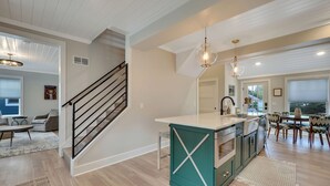 A modern kitchen with a central island, a dining area with a large window, and a staircase leading to another level. - Cherry Pie Abode | Walkable to Downtown Boyne | Pet Friendly | Hot Tub (Boyne City)