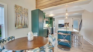 A modern kitchen with green cabinets, a dining area with a wooden table and patterned chairs, and a view of the outdoors. - Cherry Pie Abode | Walkable to Downtown Boyne | Pet Friendly | Hot Tub (Boyne City)