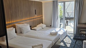 A hotel room with two beds, a wooden headboard, a large window with curtains, a patterned floor, and a small balcony area. - Hotel Carpe Diem Mostar (Mostar)
