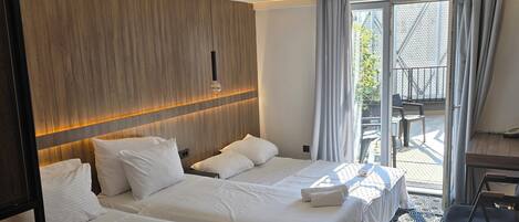A hotel room with two beds, a wooden headboard, a large window with curtains, a patterned floor, and a small balcony area.