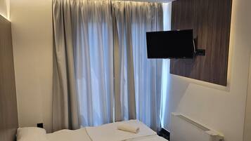 Habitación de hotel con cama, televisor de pantalla plana montado en la pared, ventana con cortinas y radiador.