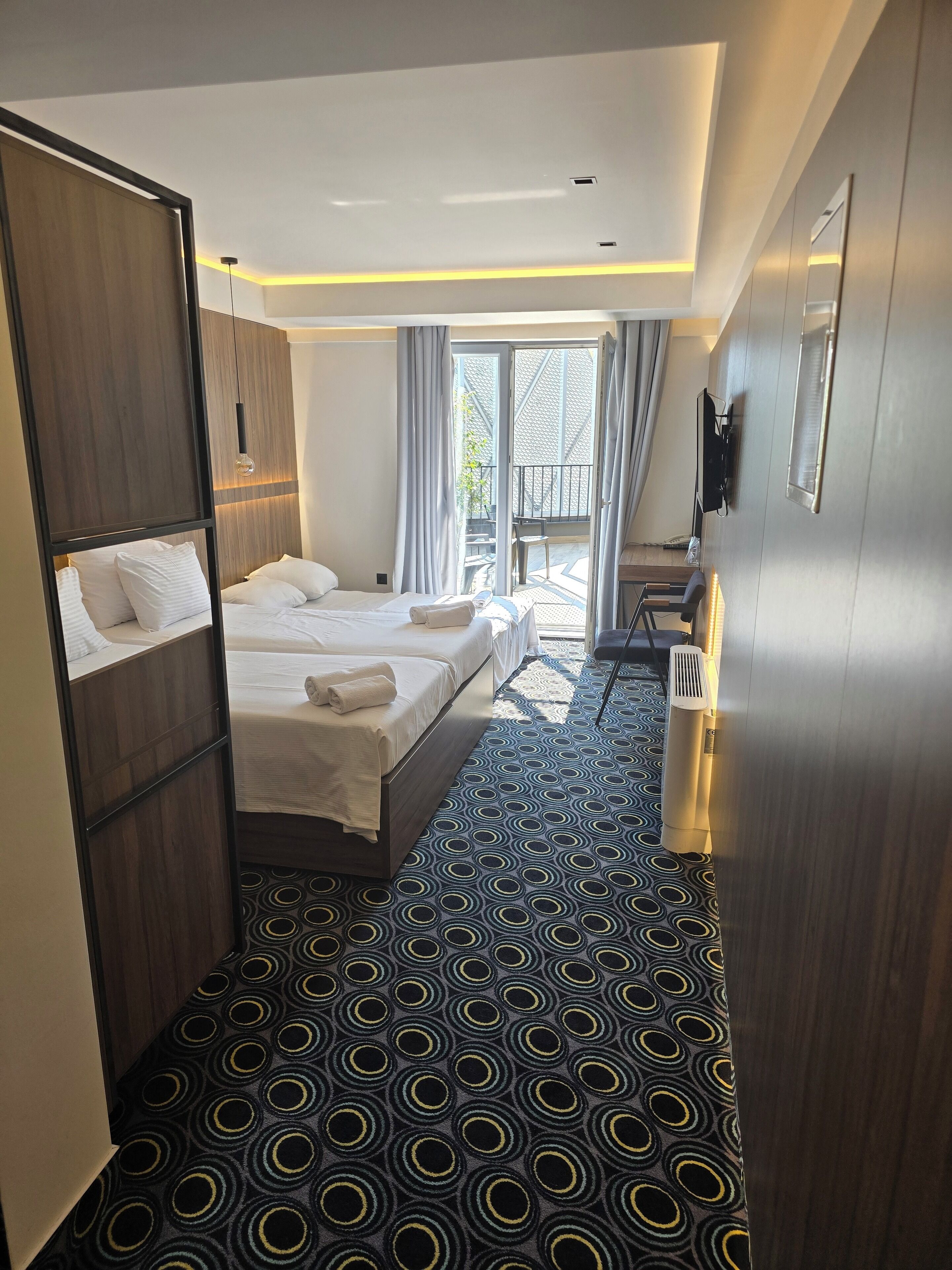 Une chambre d’hôtel avec deux lits, une grande fenêtre, un balcon et un sol à motifs.
