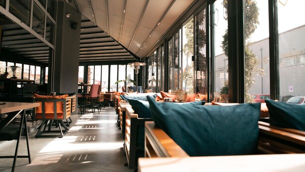 A spacious cafe with large windows, wooden tables, and comfortable seating. - Hotel Carpe Diem Mostar (Mostar)
