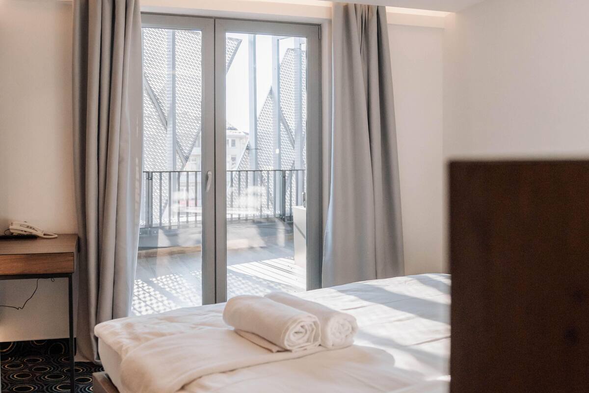 A hotel room with a bed, a desk, and a view of a balcony.