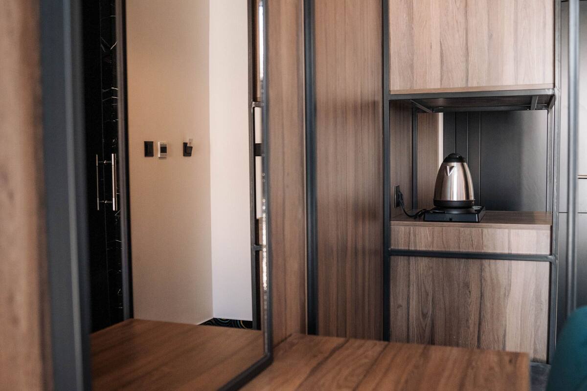A room with a wooden floor, a mirrored wardrobe, and a shelf with a kettle.