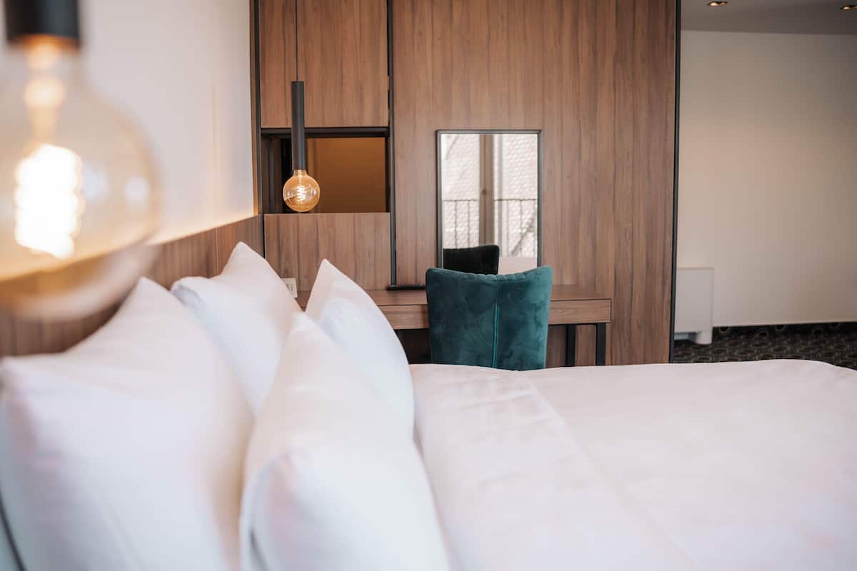 A hotel room with a large bed, a desk with a chair, a mirror, and a hanging light fixture.
