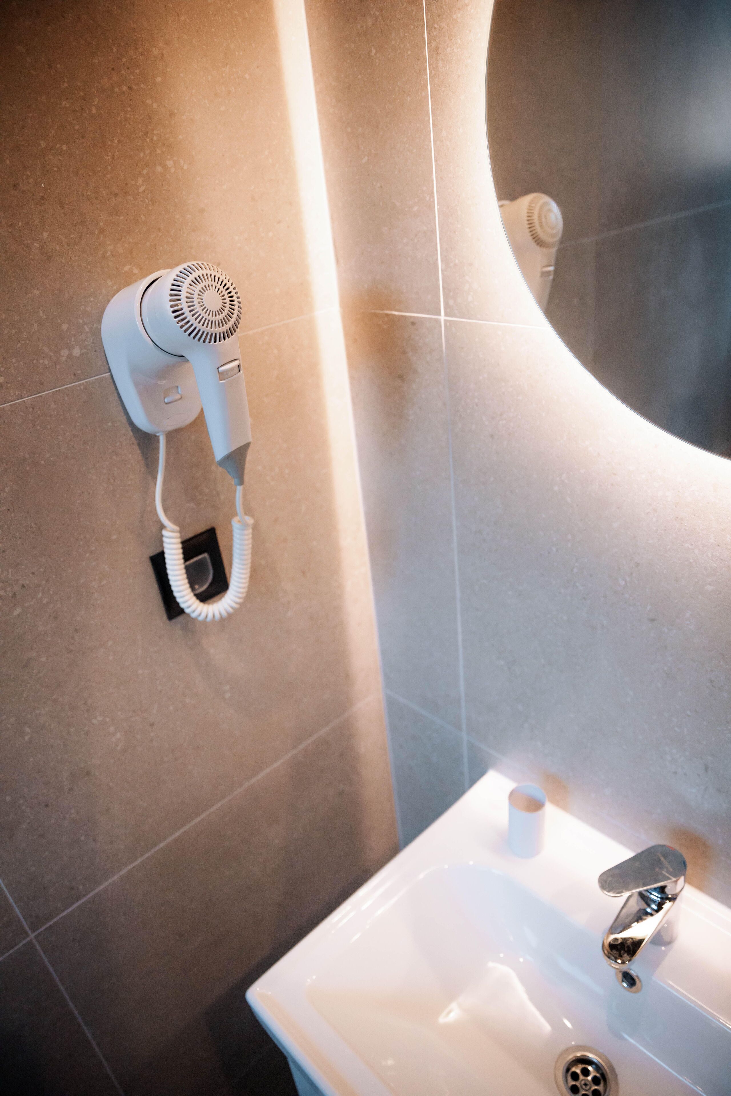 A bathroom with a white sink, a mirror, and a hairdryer mounted on the wall.