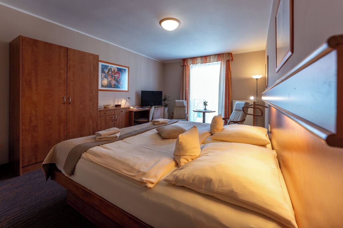 A hotel room with a large bed, a desk, a television, and a window with curtains.