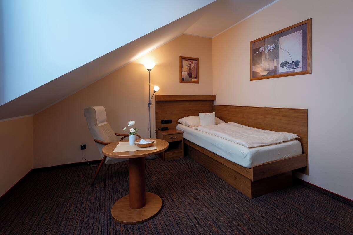A small, modern bedroom with a single bed, a chair, a table, and a lamp.