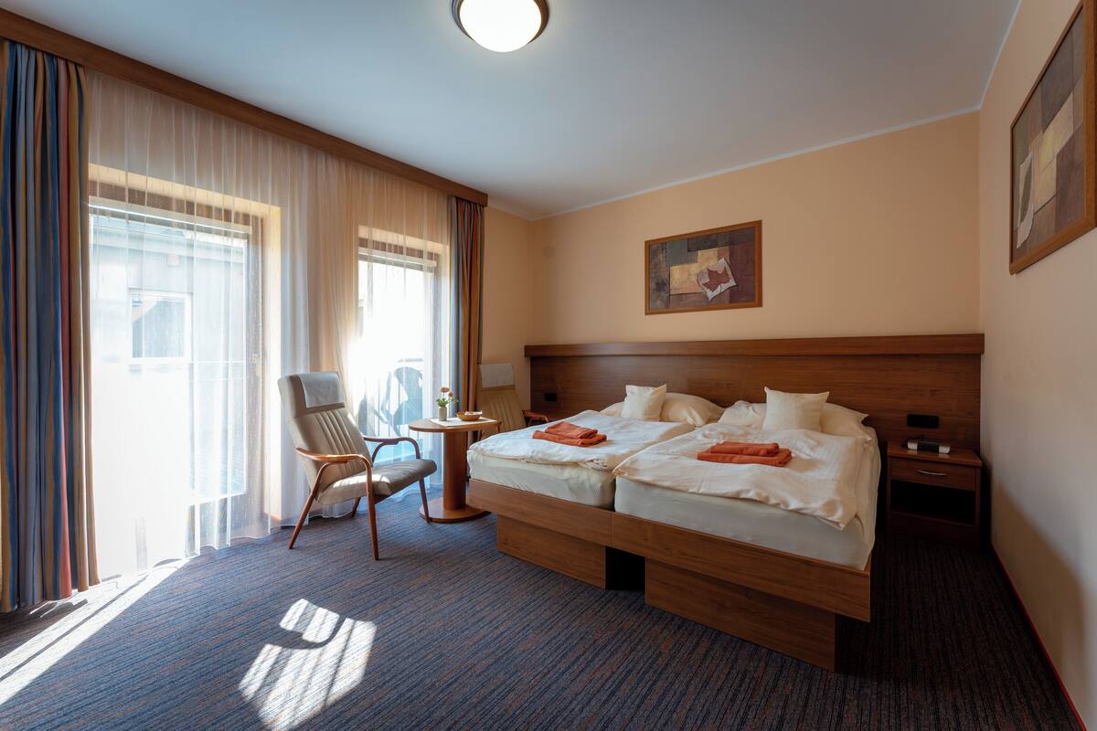 A hotel room with two beds, a chair, a small table, and a nightstand.