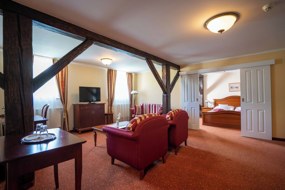 A hotel room with a wooden ceiling, a TV, a sofa, a bed, and a dining area with a table and chairs.