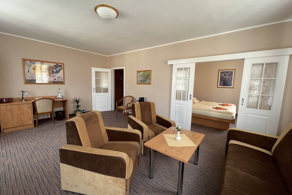 A hotel room with a bed, two sofas, a desk, a chair, and a small table.