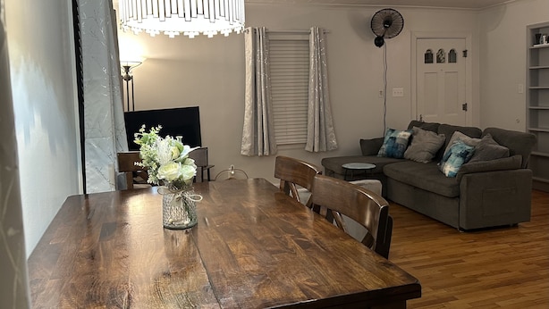 A dining area with a wooden table, chairs, a vase with flowers, a ceiling light fixture, a television, a gray sofa, and a fan. - The Walnut House - Right at OSU Greek Row and blocks from Theta Pond (Stillwater)