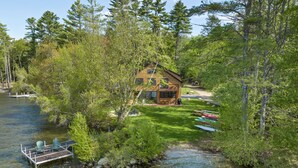Una cabaña con terraza que da a un río, rodeada de un bosque denso.