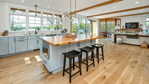 Una cocina moderna con una isla grande, taburetes de bar y una zona de comedor con televisor.