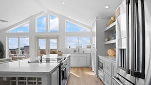 A modern kitchen with a large island, white cabinetry, and a stainless steel refrigerator. - Your Beach Retreat Awaits: Game Room, Community Pool & Easy Beach Access (Port Aransas)