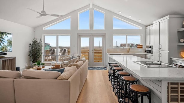 A spacious kitchen with a large island, a dining area with high-backed chairs, and a living room with a sofa and a TV. - Your Beach Retreat Awaits: Game Room, Community Pool & Easy Beach Access (Port Aransas)