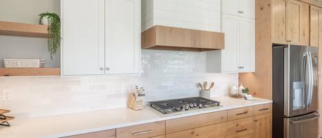 A modern kitchen with white cabinetry, a stainless steel refrigerator, and a built-in gas stove.