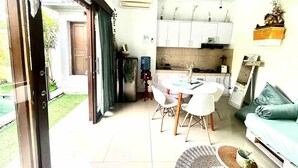 Una cocina moderna con armarios blancos, un comedor con mesa y sillas blancas, y una sala de estar con sofá y mesa de centro.