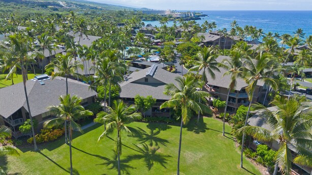 Un resort con varias edificaciones, palmeras y vista al océano.