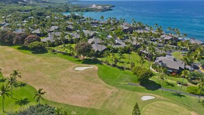 Vista aérea de un complejo turístico costero con varios edificios, palmeras y un campo de golf.