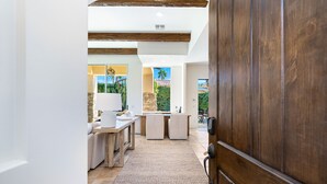 A modern interior with a wooden door, a kitchen area with a dining table, and a view of the outdoors. - HAC01 - Haciendas at La Quinta (La Quinta)