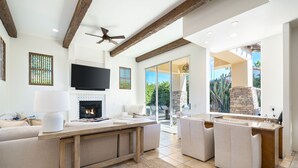 A modern living room with a fireplace, a television, and a large window overlooking a garden. - HAC01 - Haciendas at La Quinta (La Quinta)
