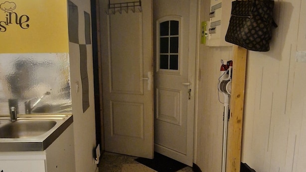 Een smalle keuken met betegelde vloer, een spoelbak en een deur naar een andere kamer.