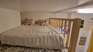 Een slaapkamer met een bed, beddengoed met een patroon, een houten hoofdeinde en een bord met namen aan de muur.