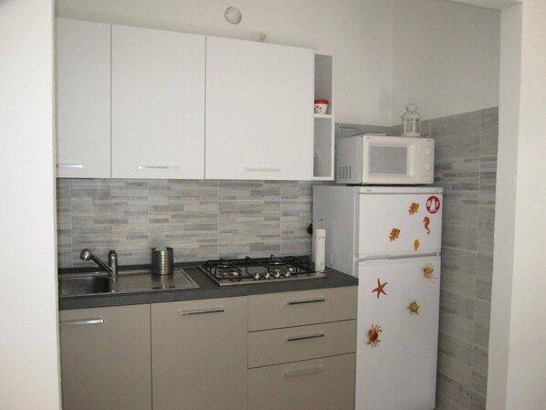 A kitchen with white cabinets, a microwave, a refrigerator, and a tiled backsplash.