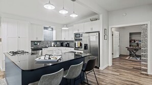 Una cocina moderna con armarios blancos, una isla central con taburetes de bar, un microondas integrado y un refrigerador de acero inoxidable.