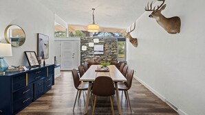 Un comedor con una larga mesa de madera, sillas marrones, una cabeza de ciervo montada en la pared y un muro de piedra detrás de la mesa.