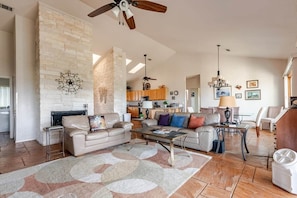 A spacious living room with a fireplace, a dining area, and a kitchen in the background.
