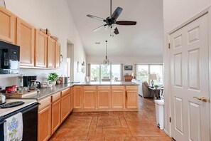 A spacious kitchen with wooden cabinets, a central island, a ceiling fan, and a view to the dining area.
