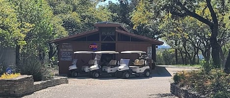 A building labeled 'PLACE' with a sign indicating it's open. There are three golf carts parked in front.