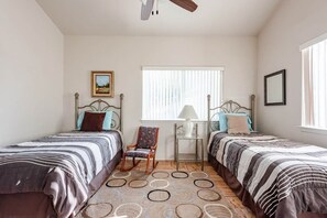 A bedroom with two beds, a chair, a lamp, and a window.