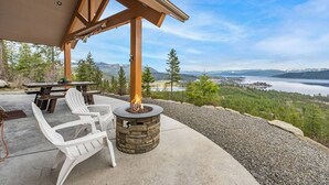 Eine Terrasse mit einem Steinkamin, weißen Stühlen und einem Tisch mit Blick auf eine malerische Berg- und Seelandschaft.