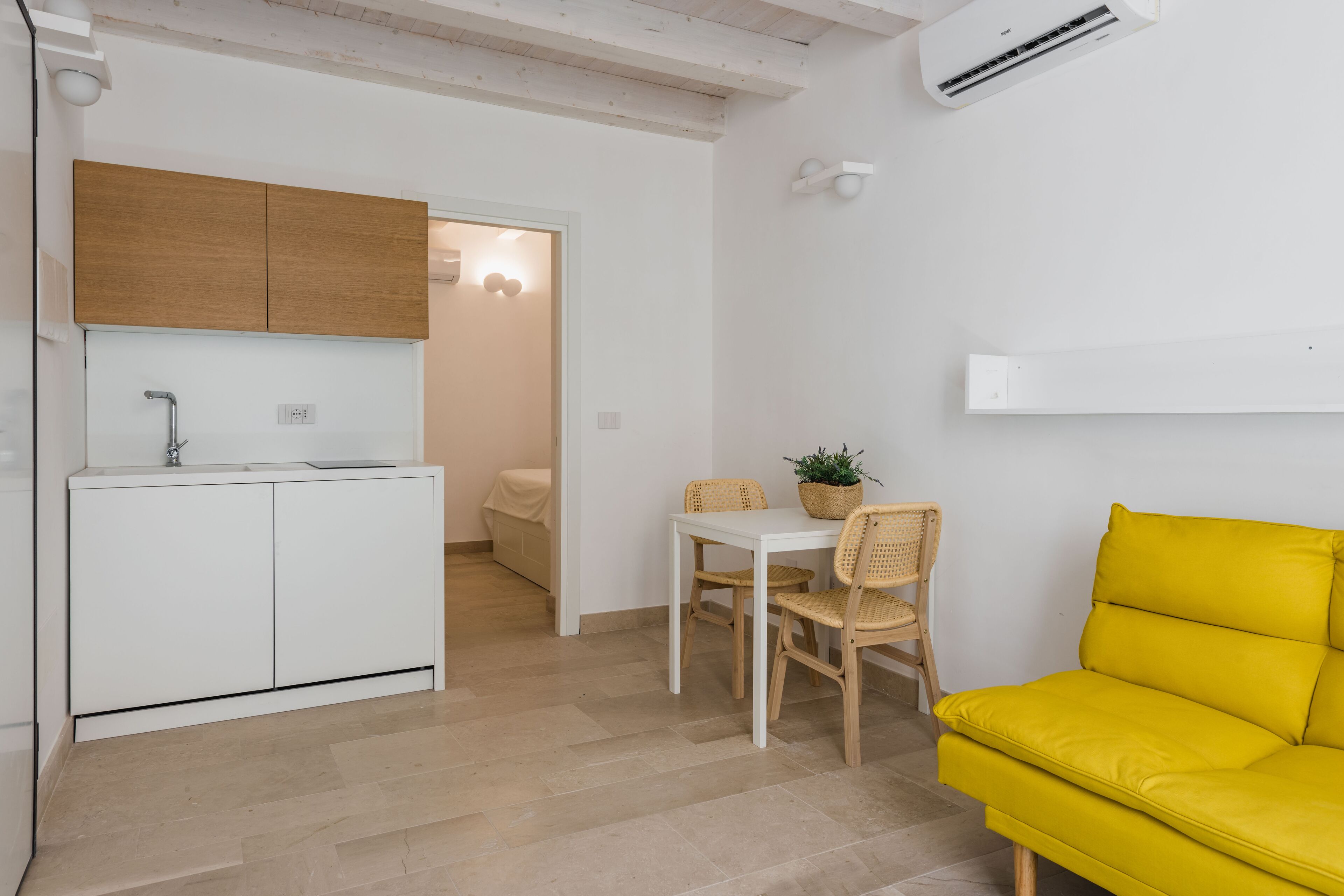 Een compacte leefruimte met een kitchenette, een eethoek en een heldergele bank.