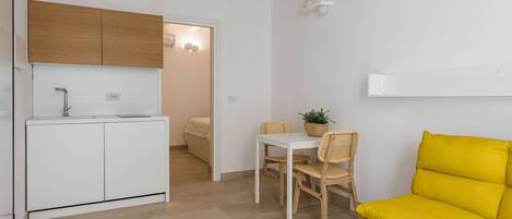 Een compacte leefruimte met een kitchenette, een eethoek en een heldergele bank.