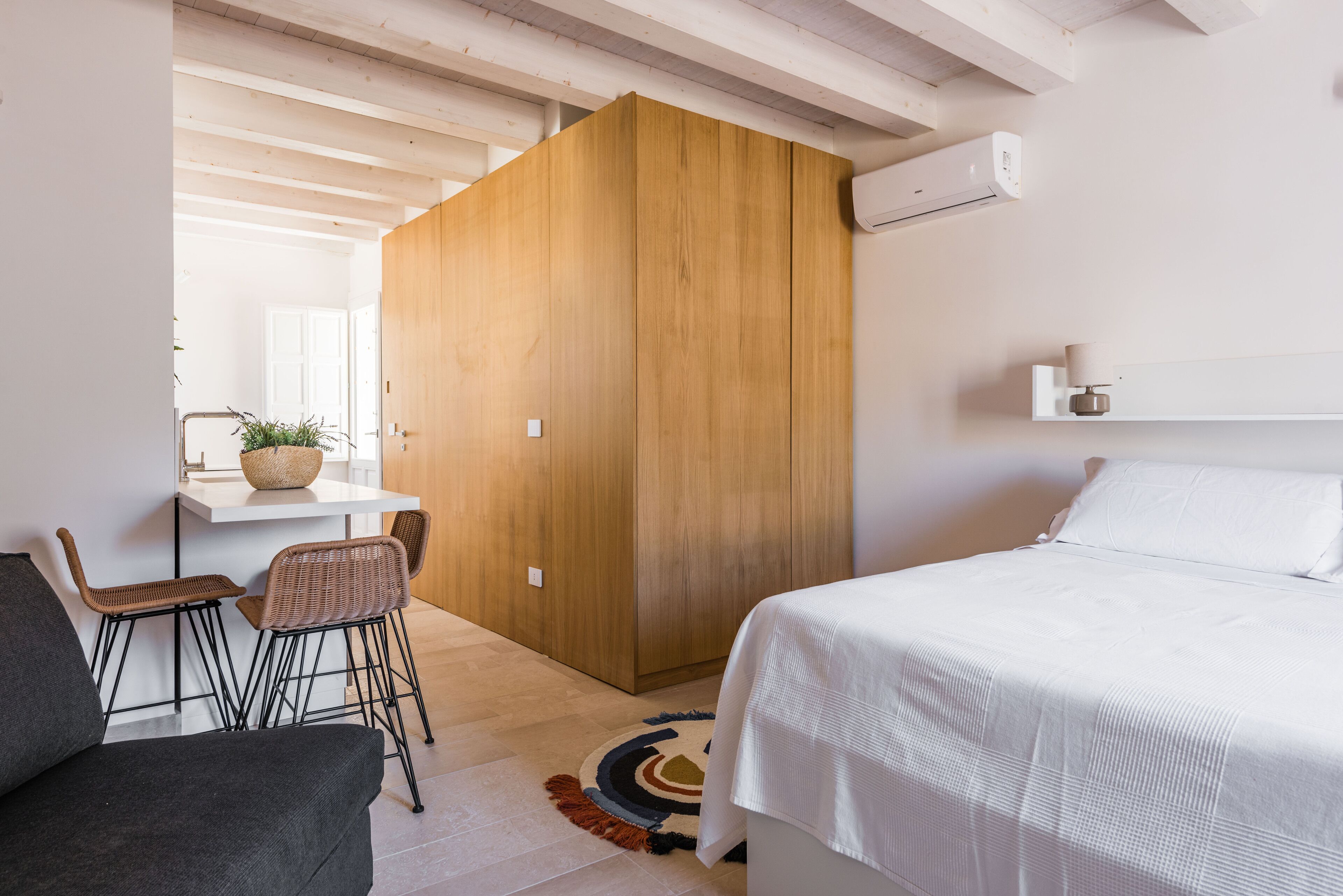 Een moderne slaapkamer met een groot bed, een houten garderobe, een klein bureau met stoel en een plant in pot.