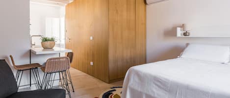 Een moderne slaapkamer met een groot bed, een houten garderobe, een klein bureau met stoel en een plant in pot.