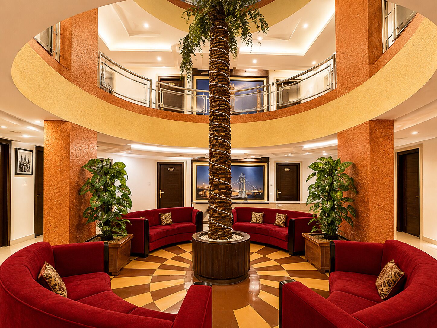 Un lobby de varios niveles con sofás rojos, una palmera central y un suelo a cuadros.