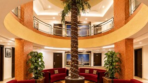 A multi-level lobby with red sofas, a central palm tree, and a checkered floor. - Hotel Europa Inn (Rajkot)