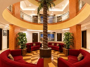 A multi-level lobby with red sofas, a central palm tree, and a checkered floor. - Hotel Europa Inn (Rajkot)