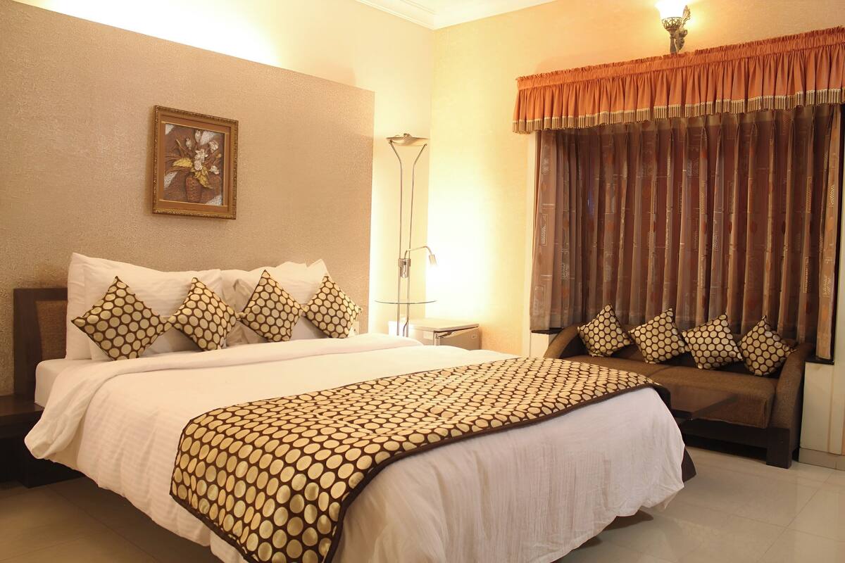 A hotel room with a large bed, a sofa, a standing lamp, and a framed picture on the wall.
