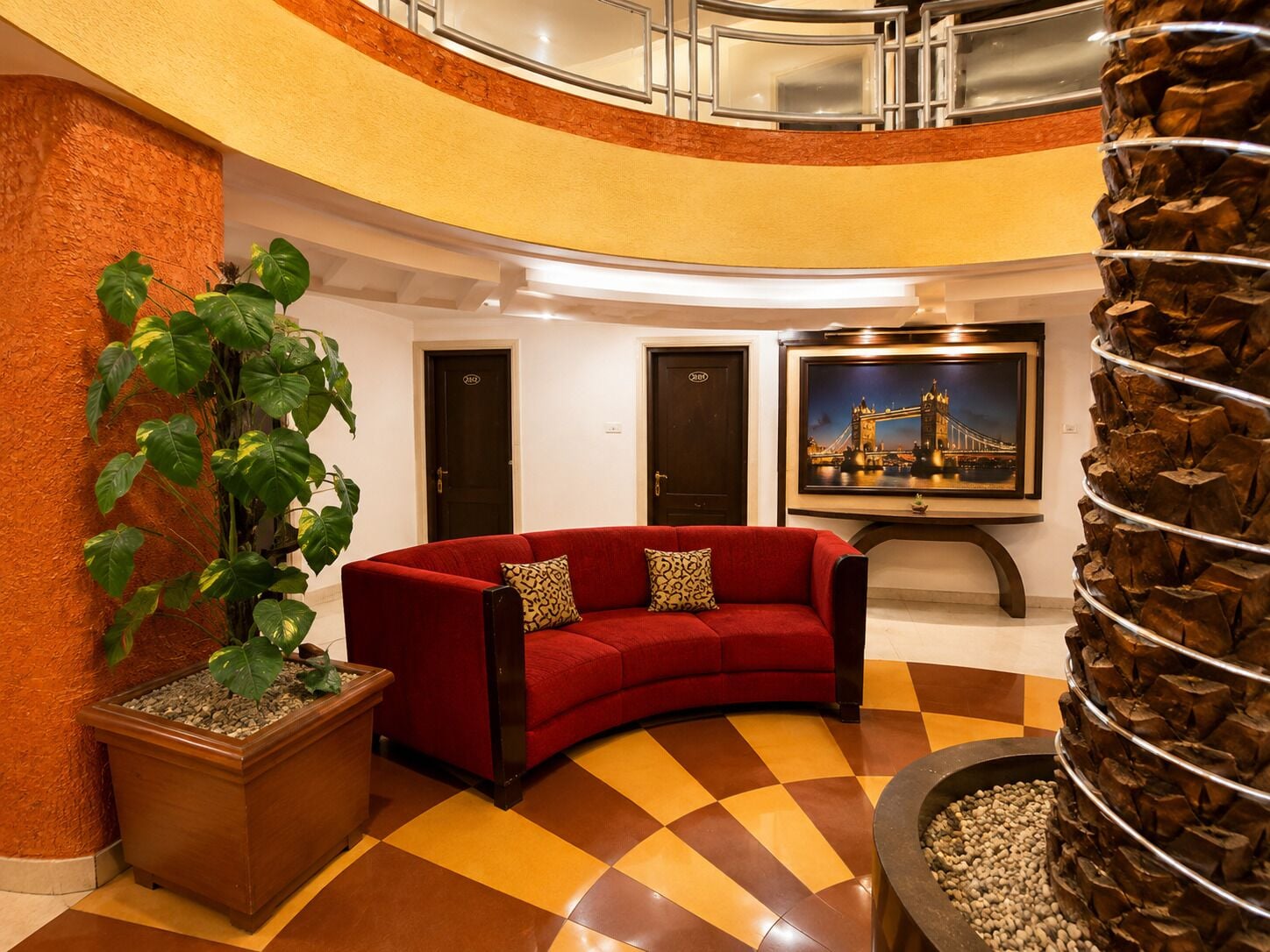 A hotel lobby with a red sofa, a large potted plant, a framed picture of a bridge, and a unique spiral column.